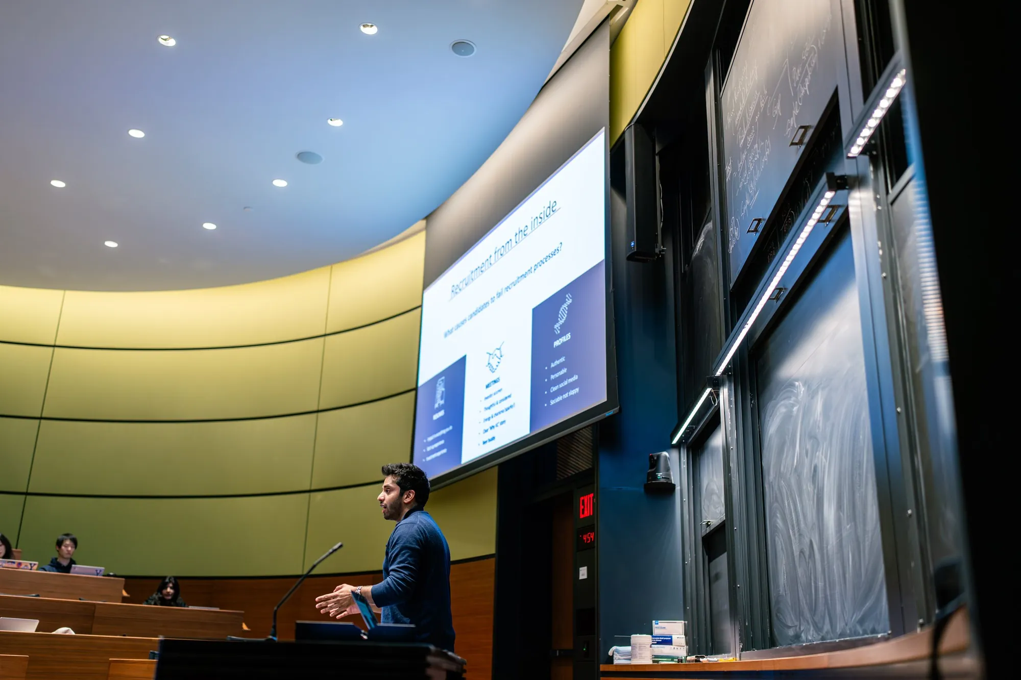 Hassan Akram presenting at a lectern in a Yale School of Management lecture theatre.